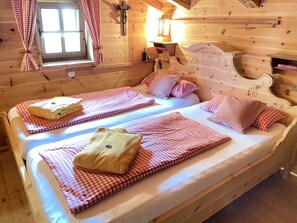 Une chambre dans une cabane en bois, avec deux lits, une literie à carreaux, une fenêtre avec des rideaux et une tête de lit en bois.