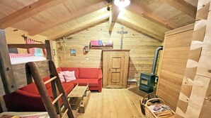 A cozy attic room with a wooden ceiling, a red sofa, a wooden ladder, a small table, and a basket of items. - Bayerisches Refugium mit Sauna (Tittmoning)