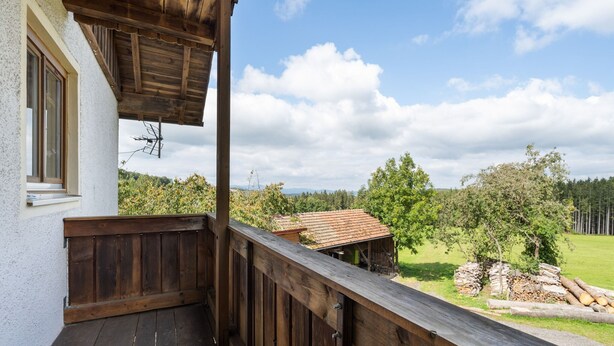 Een houten balkon met uitzicht op een landelijk landschap, met bomen en een gebouw in de verte.