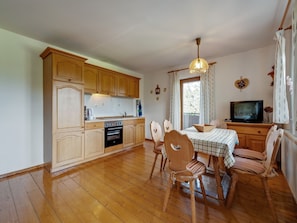 Cocina compacta con armarios de madera, horno empotrado y comedor con mesa y sillas.