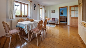 Een eetgedeelte met een tafel voor vier personen, houten stoelen, een hanglamp en uitzicht op een slaapkamer met een bed en een kledingkast.
