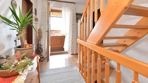 Een houten trap die leidt naar een verdieping, een plant in een pot en een deur naar een balkon met een houten hek.