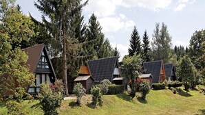 Una hilera de casas de madera tradicionales con techos pronunciados, rodeadas de un bosque denso y céspedes bien cuidados.