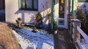 Un edificio con fachada blanca y detalles en verde, una puerta con un pequeño ventanal y suelo cubierto de nieve.