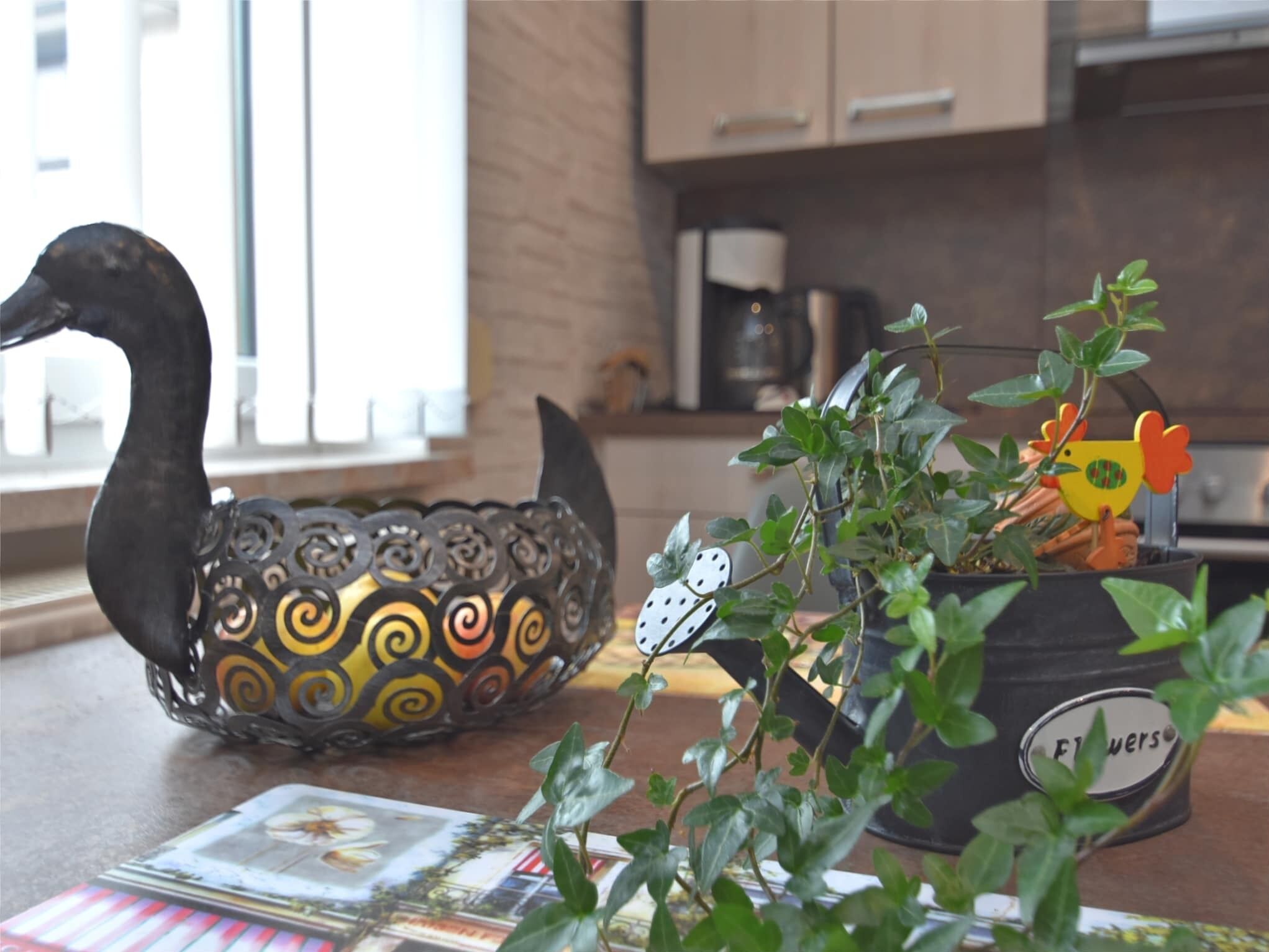 A kitchen counter with a decorative metal swan, a potted plant with a flower pot, and a magazine.
