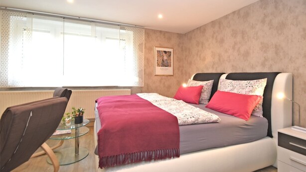 Un dormitorio moderno con una cama grande, una mesa de centro de vidrio, una silla y una mesita de noche.
