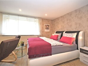 Un dormitorio moderno con una cama grande, una mesa de centro de vidrio, una silla y una mesita de noche.