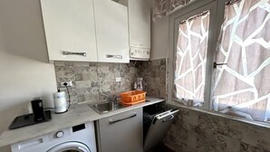 A compact kitchen with a washing machine, a sink, and a window with patterned curtains. - The "Cenerone" - Comfort and Relax, discover sea and country, feel our culture (Borgo Santa Maria Immacolata)
