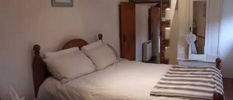 Un dormitorio con una cama, una mesita de noche, un espejo y una puerta que da a otra habitación.