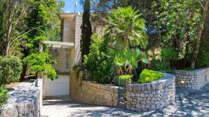 A stone-walled garden with a palm tree, a white door, and a stone pathway leading to a building with a tiled roof. - Villa in Alcúdia near Sandy Beach (Alcudia)