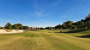 A golf course with sand bunkers, trees, and modern buildings in the background. - Golfside Luxury at Las Colinas (Orihuela Costa-Alicante)