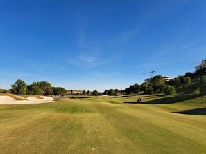 Golfkenttä, jossa on hiekkabunkkereita, puita ja taustalla moderneja rakennuksia.