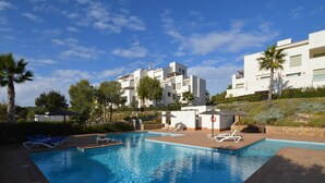 A swimming pool with lounge chairs, a lifeguard stand, and a small poolside area with a bench. - Golfside Luxury at Las Colinas (Orihuela Costa-Alicante)
