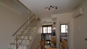 A modern kitchen with a dining area, a staircase, and an air conditioning unit.