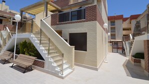 A modern building with a staircase leading to a second floor, surrounded by a courtyard with benches and a bike rack.