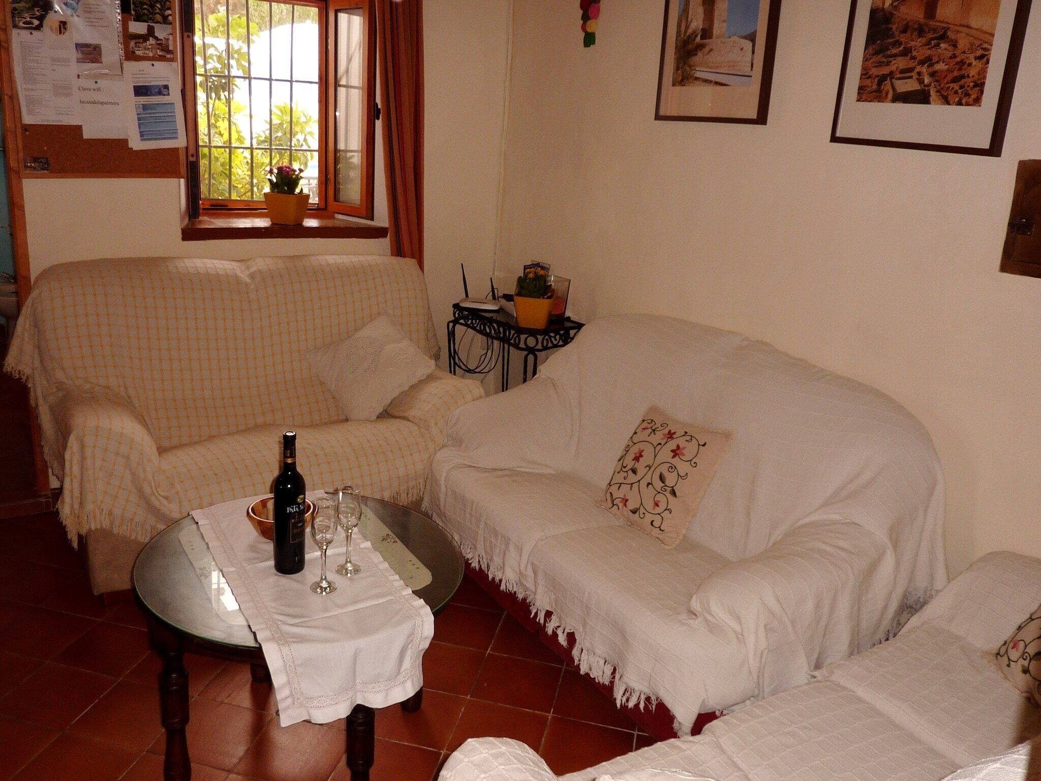 A living room with a checkered sofa, a small table with a bottle and glasses, and a window with curtains.