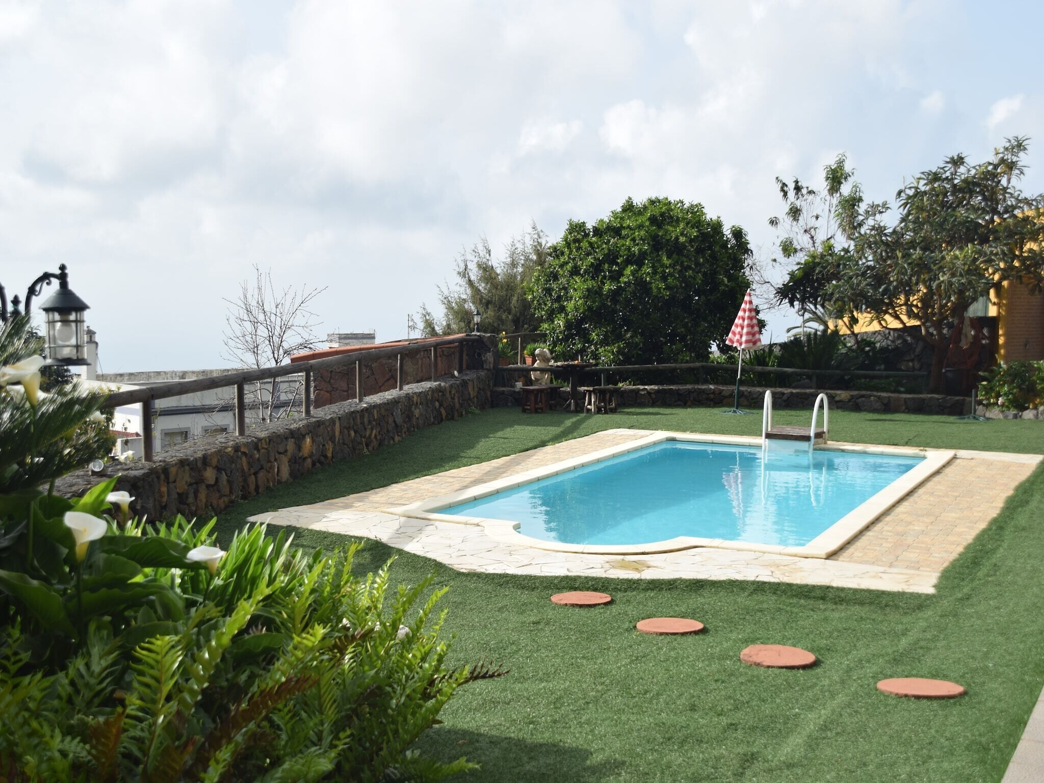 A swimming pool with a stone border, surrounded by artificial grass and a stone wall.