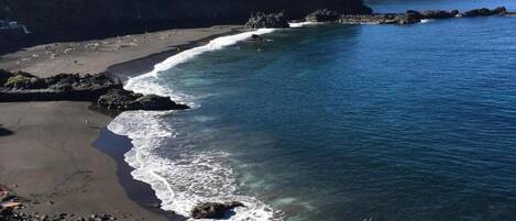 A coastal landscape with a sandy beach, rocky shoreline, and clear blue water.