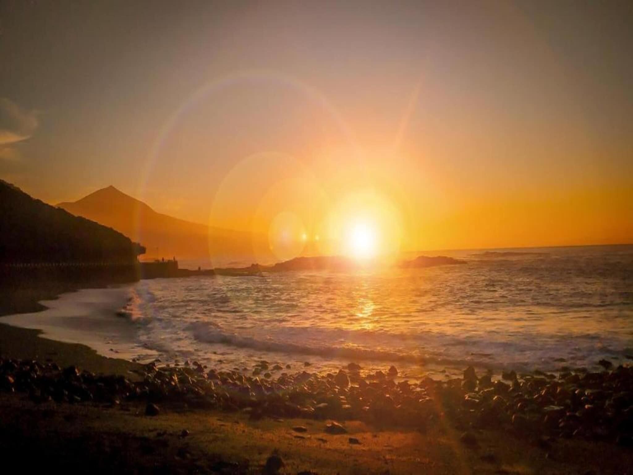 A sunset over the ocean with a mountain in the background.