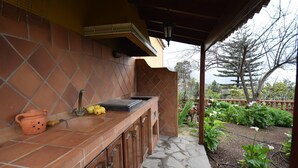 Una cocina con encimera de piedra, un lavamanos y una olla colgando. Se ve un jardín a través de la ventana.