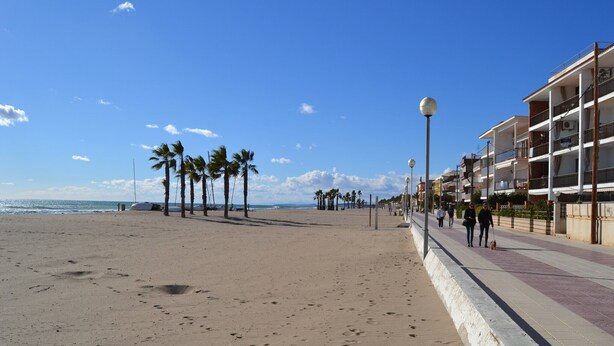 A beach with a promenade, palm trees, and a building with balconies. - Holiday Home in Vendrell near Costa Dorada Beach (El Vendrell)