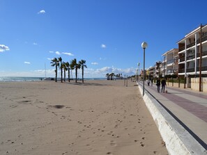 A beach with a promenade, palm trees, and a building with balconies.