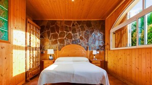 A wooden bedroom with a stone wall, a bed, two bedside tables, and a window with a view of greenery. - Holiday Home in Vendrell near Costa Dorada Beach (El Vendrell)