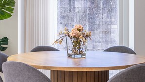 A dining area with a round wooden table, six grey upholstered chairs, a hanging blue pendant light, and a vase with flowers on the table. - Mexia Galvao - City Center, Mexia Galvão - City Center (Viana do Castelo)