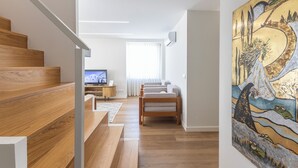 A modern interior with a wooden staircase, a living area with a sofa and TV, and a painting on the wall. - Mexia Galvao - City Center, Mexia Galvão - City Center (Viana do Castelo)