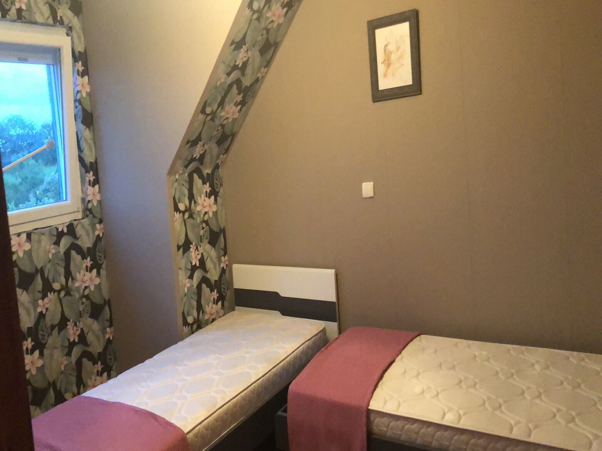 Een kleine kamer met twee bedden, een raam met uitzicht en een lijst met een foto aan de muur.