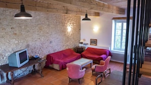 A rustic room with stone walls, a wooden ceiling, a television, two beds with red covers, and a table with chairs. - Holiday Home in Béziers with Pool and Vineyard (Murviel les Béziers)