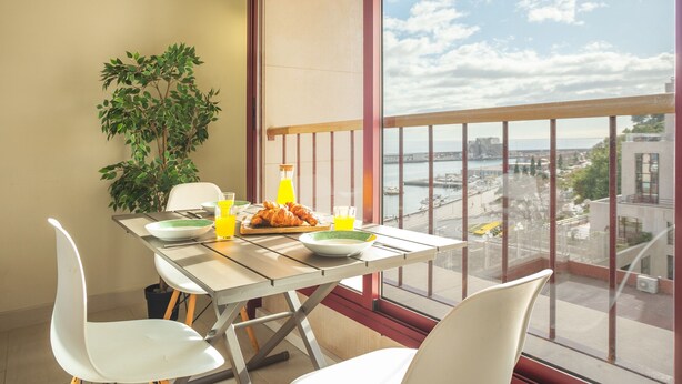 A dining area with a table set for two, a plant, and a view of a cityscape through large windows. - Tropical Sun by Atlantic Holiday (Funchal)
