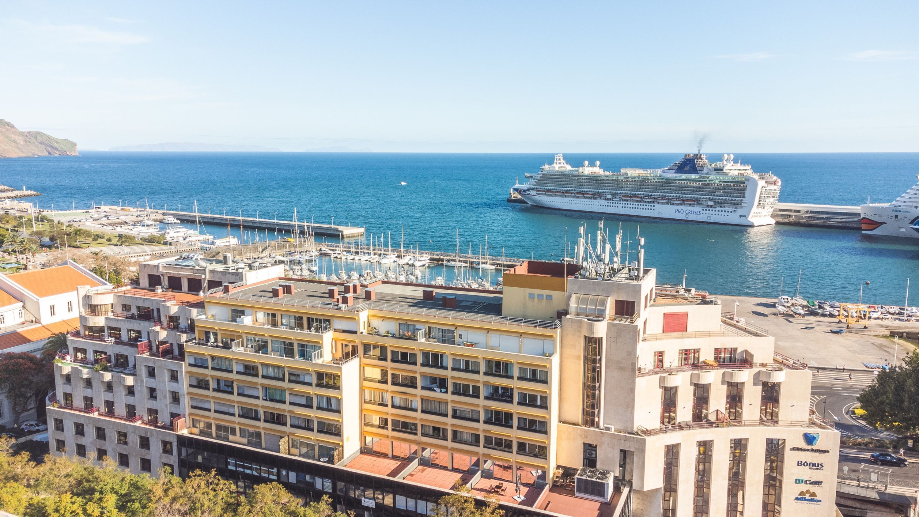 A cruise ship docked at a marina with a cityscape in the background.