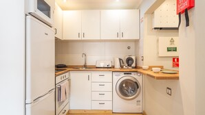 A compact kitchen with white cabinets, a built-in oven, a washing machine, and a microwave. - Tropical Sun by Atlantic Holiday (Funchal)
