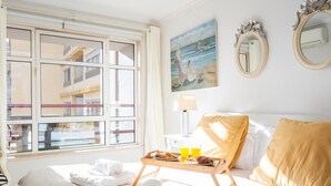 A hotel room with a bed, a window with a view of buildings, a painting on the wall, and a tray with breakfast items. - Tropical Sun by Atlantic Holiday (Funchal)
