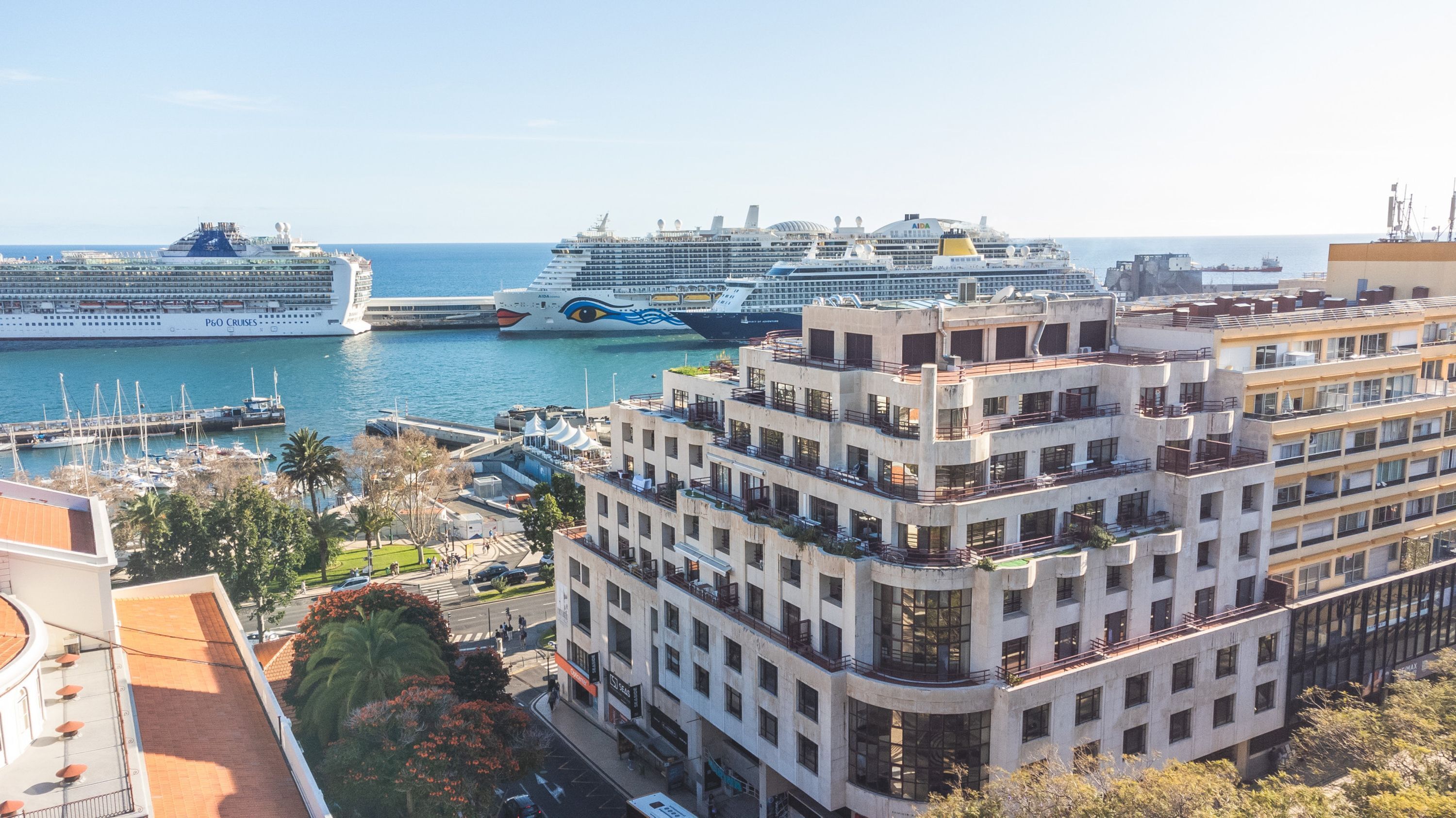 Un paysage urbain côtier avec des bâtiments modernes, une marina où sont amarrés des navires de croisière et une vue dégagée sur la mer.