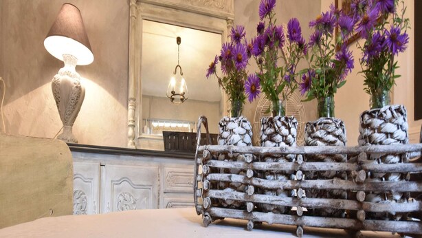 A room with a white fireplace, a mirror above it, and a wooden log bench with vases of purple flowers.