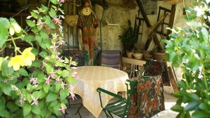 A rustic outdoor dining area with a round table covered by a floral tablecloth, surrounded by green chairs and baskets.