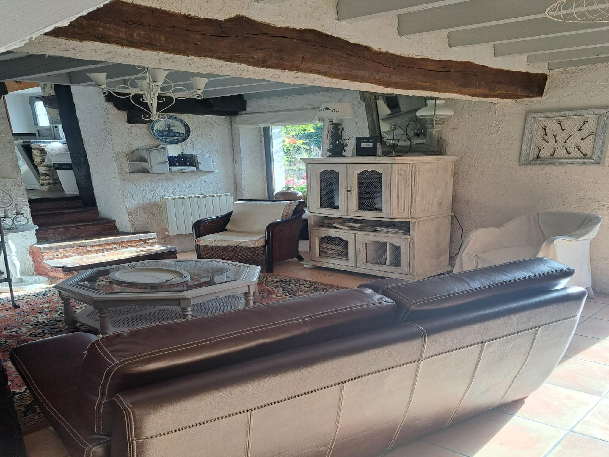Ein Wohnzimmer mit einem braunen Ledersofa, einem weißen Sessel, einem Holzschrank und einem gemusterten Teppich.