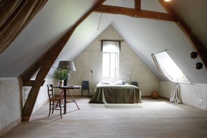 Et værelse med skråvæg, en seng med grønt sengetæppe, en stol, et bord med en lampe og et vindue.