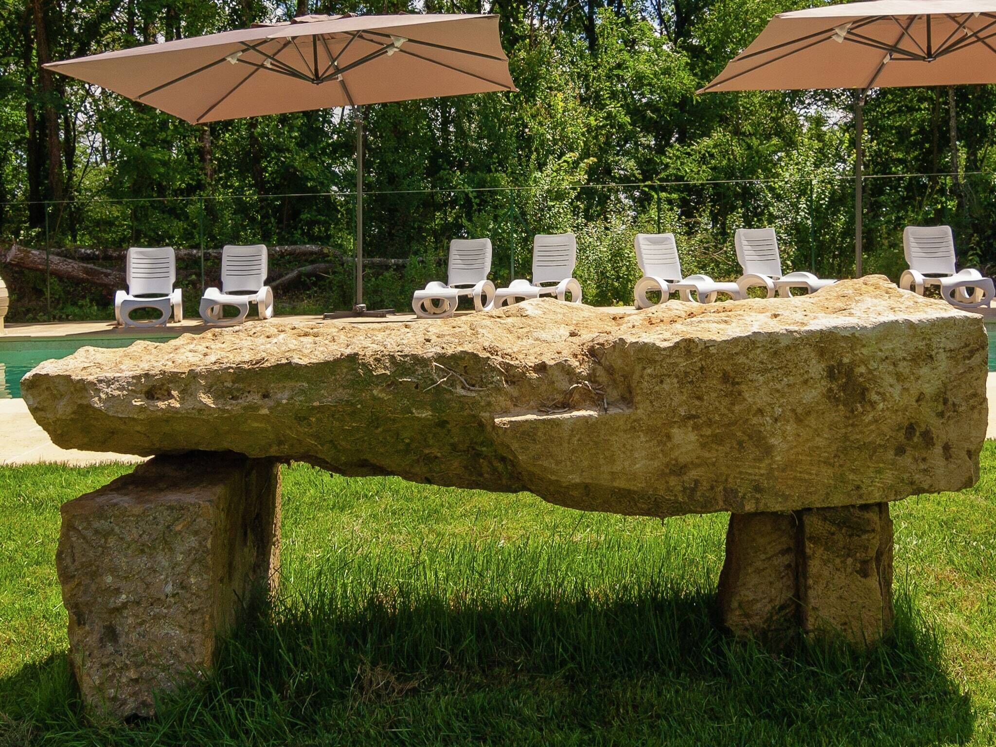 A stone bench with white plastic chairs and umbrellas in a grassy area.