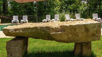 A stone bench with white plastic chairs and umbrellas in a grassy area.