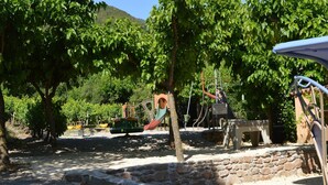 A playground with various play structures, surrounded by trees and a stone wall. - Villa Overlooking Les Vans Centre (Les Vans)