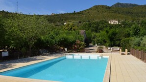 A rectangular swimming pool with a tiled deck, surrounded by lush greenery and a mountainous backdrop. - Villa Overlooking Les Vans Centre (Les Vans)