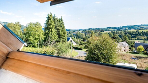 Uitzicht vanuit een raam met houten kader, over een landelijk gebied met huizen, bomen en een weg.