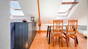 Een compacte, goed verlichte kamer met een houten eettafel en stoelen, een klein kastje en een dakraam.