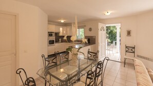 A modern kitchen with white cabinets, a glass dining table with metal chairs, and a view of the outdoors.