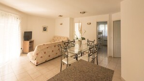 A living room with a sofa, a dining table with chairs, a television, and a potted plant.