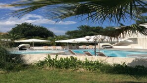 A pool area with lounge chairs and umbrellas, surrounded by greenery and palm trees. - Holiday Home in Moriani-Plage near Beach (Moriani Plage)