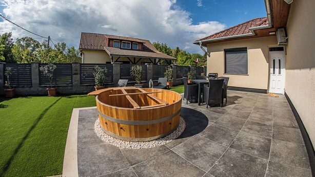 Une terrasse agrémentée d’une barrique en bois, d’un barbecue et d’un espace salon abrité.